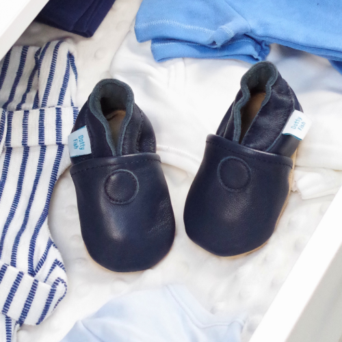 Plain navy leather baby shoes in drawer with baby clothing.
