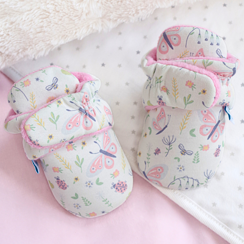 Cream baby booties with floral pattern, sitting on baby blanket.