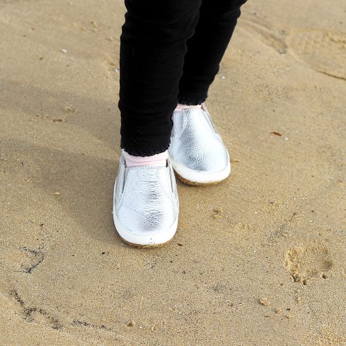 Little girl on beach wearing Dotty Fish silver leather pre-walker rubber sole slip-on shoes.