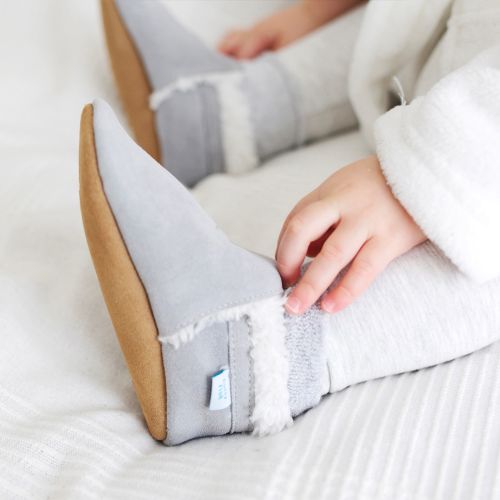 Small child on bed, wearing Dotty Fish grey suede slippers.
