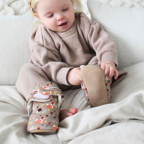 Girl wearing pale brown cotton booties with woodland pattern.