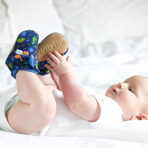 Baby wearing navy cotton booties, with dinosaur design.
