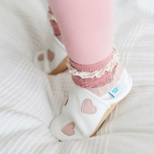 Baby wearing white leather Dotty Fish first walker barefoot shoes with pink hearts.