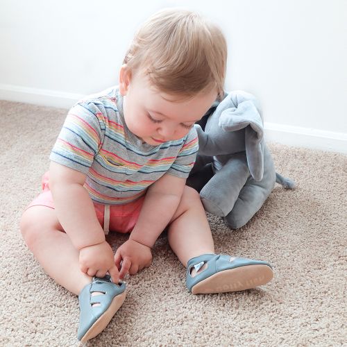 Baby boy sitting on floor, wearing grey Dotty Fish barefoot sandals.