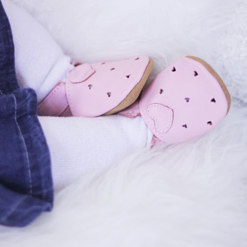 Baby wearing pink leather baby shoes with cut-out hearts.