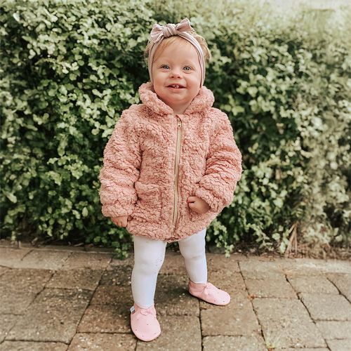 Toddler wearing pink soft leather baby shoes with cut-out hearts.