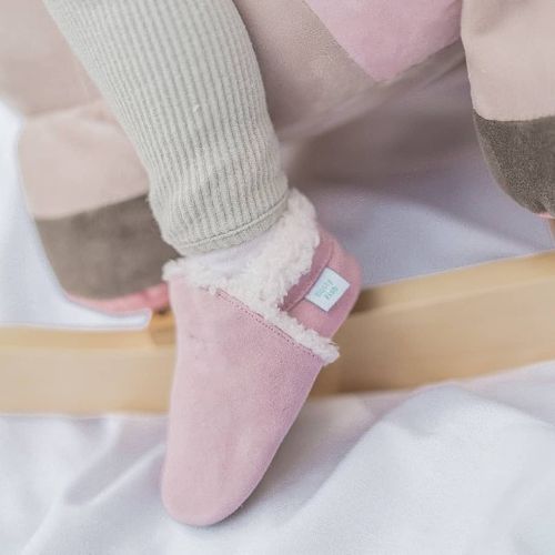 Toddler girl sitting on rocking horse, wearing pale pink suede Dotty Fish children’s slippers.